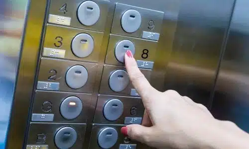 A closeup of an elevator panel with a woman's hand pressing a button.