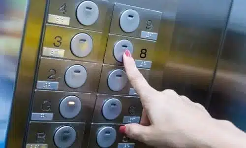 A closeup of an elevator panel with a woman's hand pressing a button.