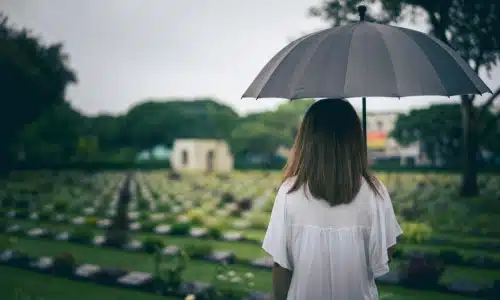 A woman standing and mourning at a funeral while holding a black umbrella.