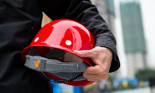 A blue collar worker with his red hardhat held under his arm.