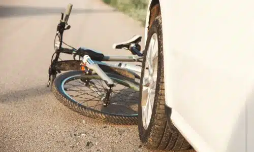 A white bicycle stuck betweent the road and the front bumper of a car.