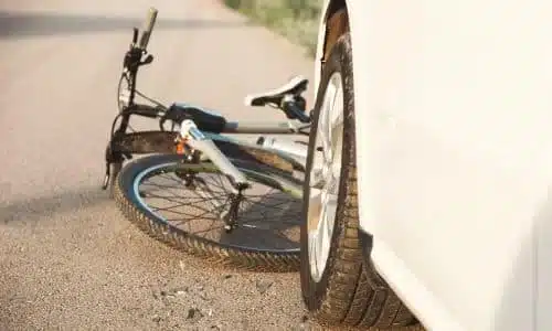 A white bicycle stuck betweent the road and the front bumper of a car.