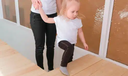 Daycare staff assisting a toddler up a set of stairs.