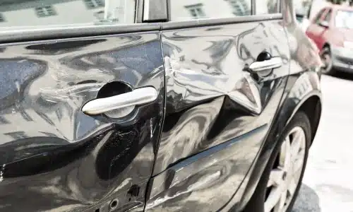 A crumpled driver's side of a dark-colored car damaged by a hit and run.