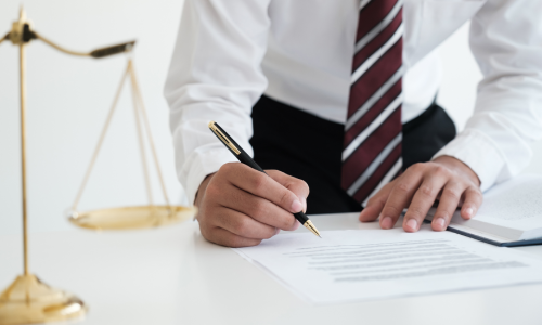 A personal injury lawyer hunched over a desk and signing documents for a case.