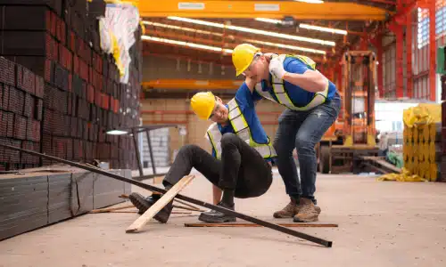 A hardhat worker helping up a coworker with an injured leg.