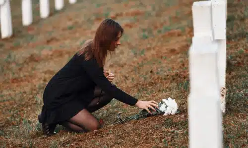 A woman mourning a wrongful death victim at a tombstone in a cemetery.