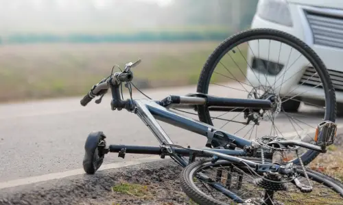 A bicycle tipped on its side after a head-on collision with a white vehicle.