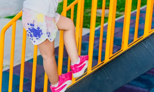 A toddler dangerously climbinb up a set of stairs from outside the rails.
