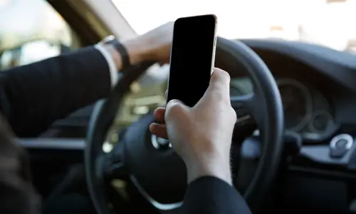A distracted driver holding her phone in her right hand while she drives her vehicle.
