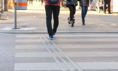 Pedestrians traversing a crosswalk in a city in the late afternoon.