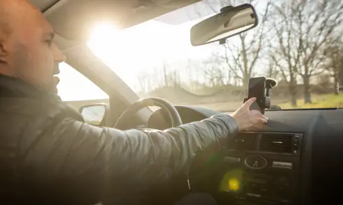 A rideshare driver adjusting his GPS system while he drives through a suburb.