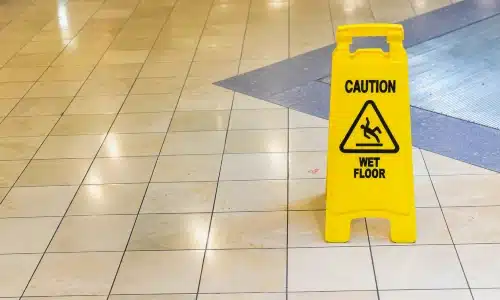 A yellow wet floor hazard sign placed on a tile floor in a building.