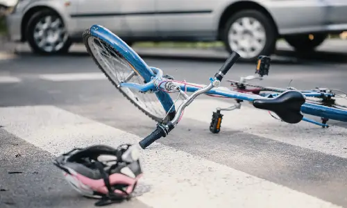 A blue bicycle on its side on a pedestrian crossing after colliding with a grey car.