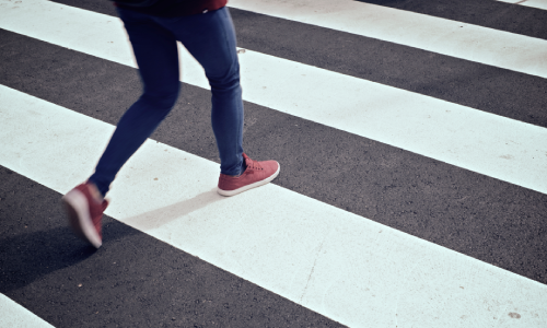 A woman in jeans running across a pedestrian crossing before vehicles arrive.