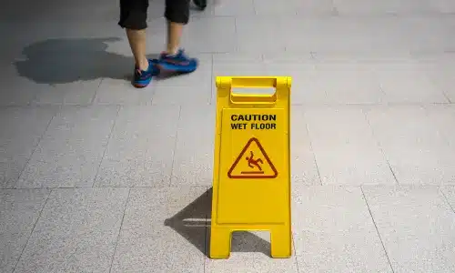 People walking on a platform next to a yellow wet floor sign.