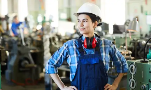 A hardhat worker with hands on his waist as he stands in a factory.