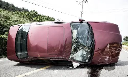 A maroon car with a sunroof turned on its side after a car accident.