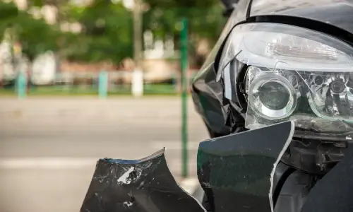 A damaged headlamp and bumper of a dark colored car stopped after an accident.