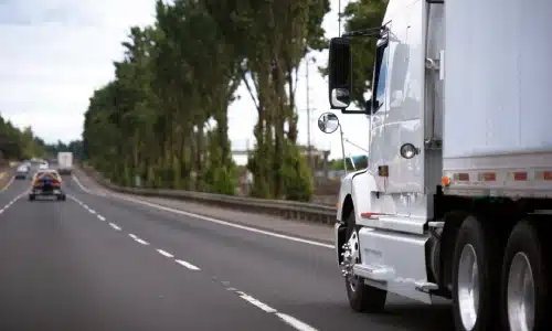 A white semi truck driving on a road and catching up with traffic in the distance.