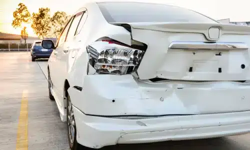 A white car with a crumpled rear end and missing license plate after an accident.