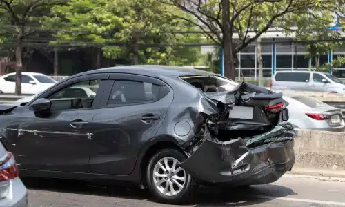 A parked black car with a crushed trunk caused by a car accident.