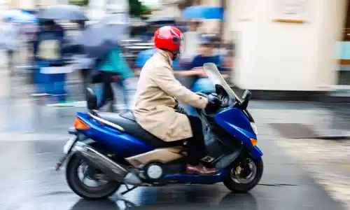 A man on a motor scooter driving at speed througha  city street.