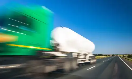 A motion-blurred image of a green truck pulling a fuel tank at speed.