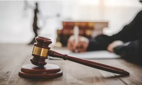 A selective focus image of a lawyer seated at a desk and filling up documents for a client's claim.