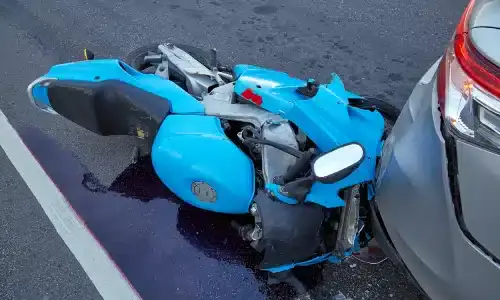 A bright blue motorcycle lying on its side after colliding with a car.