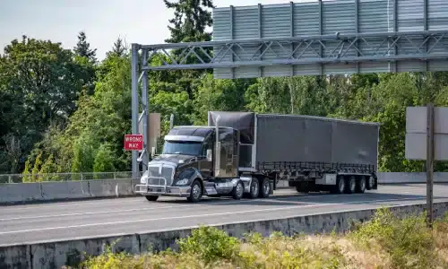 A large grey semi truck pulling a trailer along a highway.
