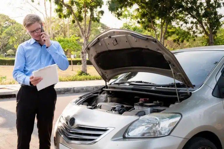 A man is on the phone after a car accident, looking at insurance information. 