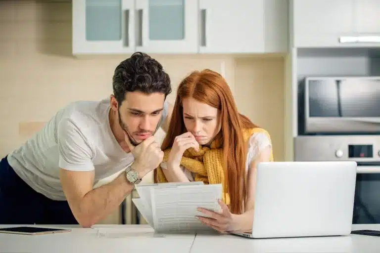 A couple reviews accident documents next to an open laptop, searching for traffic accident reports. 