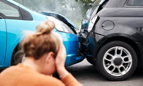 A woman by the roadside holding her head after a car accident with another vehicle.