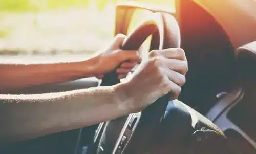 A near shot of a driver's hands on the steering wheel of their car.