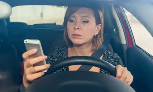 A woman holding up her hand to text another person while driving.