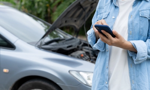 A woman contacting the police after an accident and her car in the background with the hood up.