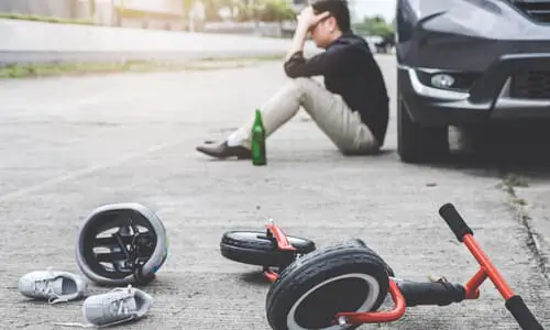 A children's tricycle, helmet, and shoes scattered on the street after a collision by a drunk driver in the background.