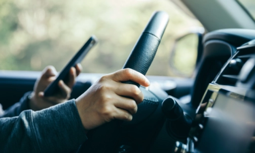 A person texting with his left hand while driving his vehicle.