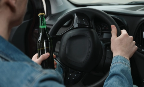 A person operating a vehicle while holding a bottle of alcohol in his left hand.