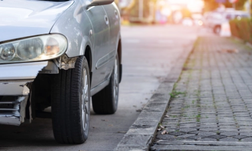 A grey car with a front bumper destroyed in a hit and run accident.