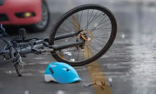 A bicycle and blue cycling helmet in the middle of the road with a car in the background.