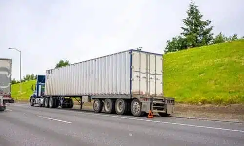 A big rig truck with an early warning device deployed stuck on the side of a highway.