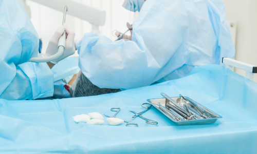 Medical tools on a tray with hospital staff in the background operating on a patient.