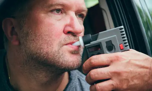 A drunk driver being administered a breathalyzer test by a police officer.