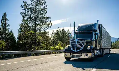 A black semi trailer truck driving along a highway on a sunny afternoon.