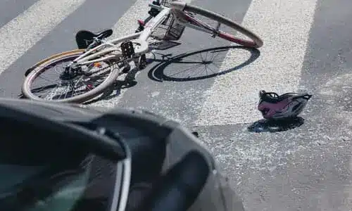 A bicycle and a cyclist's helmet lying on the a crosswalk behind a sedan after a collision.