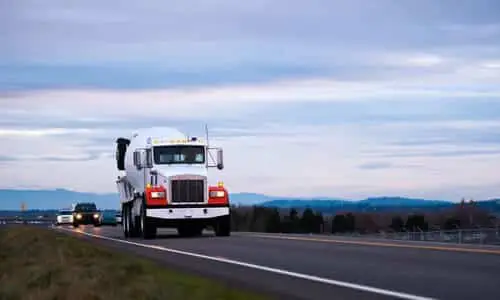 A large truck carrying an oil tank on a highway in the early evening.