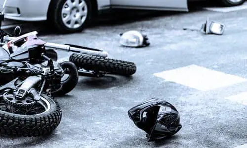 A collision between a motorcycle and a vehicle with a helmet lying on the road.