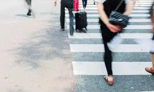 A motion-blurred image of pedestrians at a crosswalk making their way across a street.